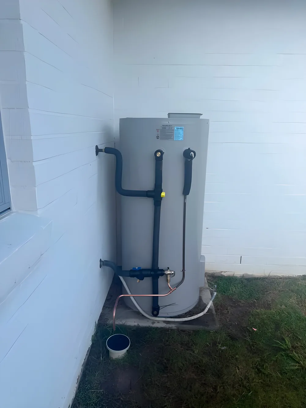 Electric hot water unit installed beside a white block wall