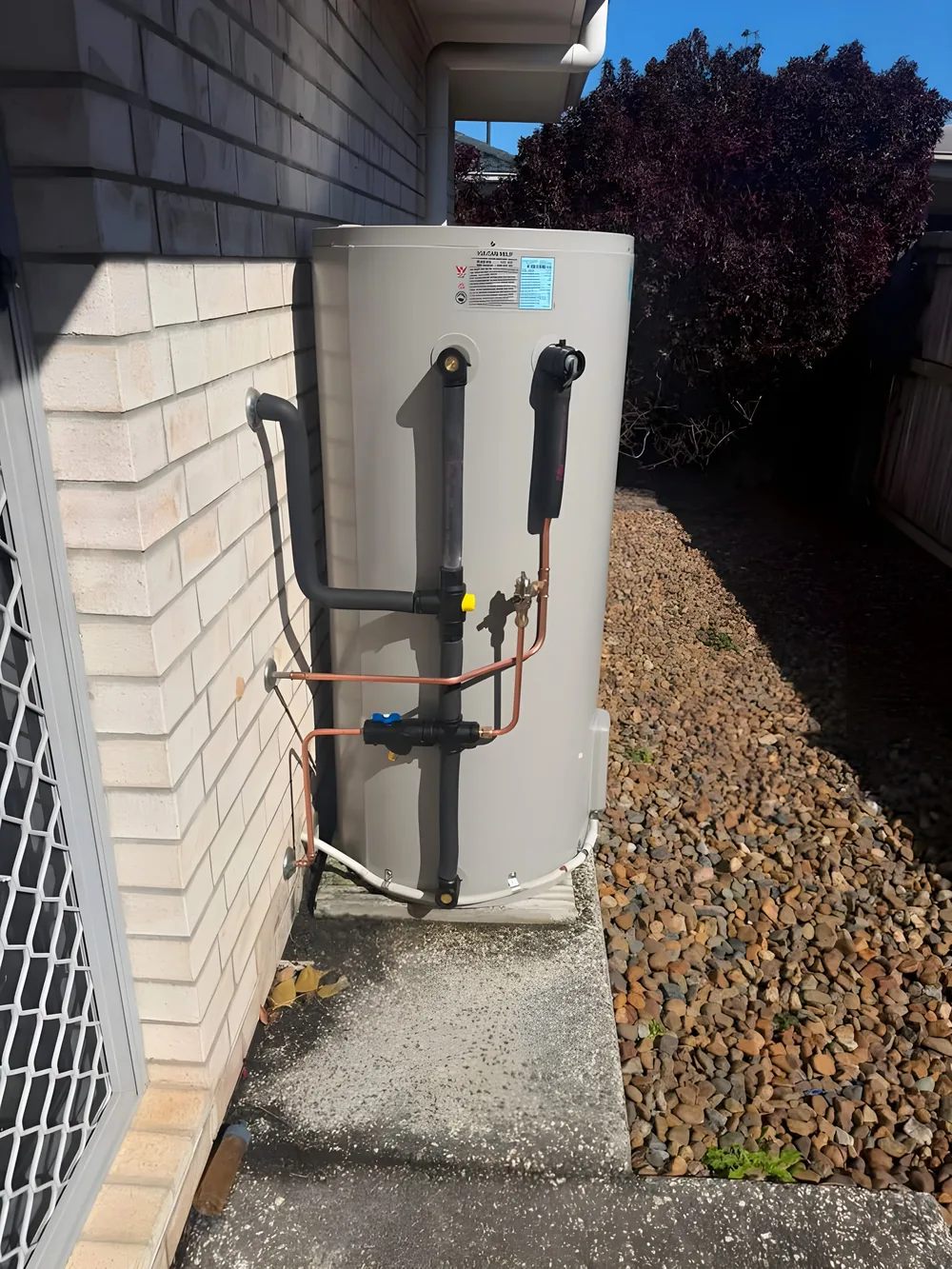 New electric hot water unit installed against a brick wall with copper and black pipework