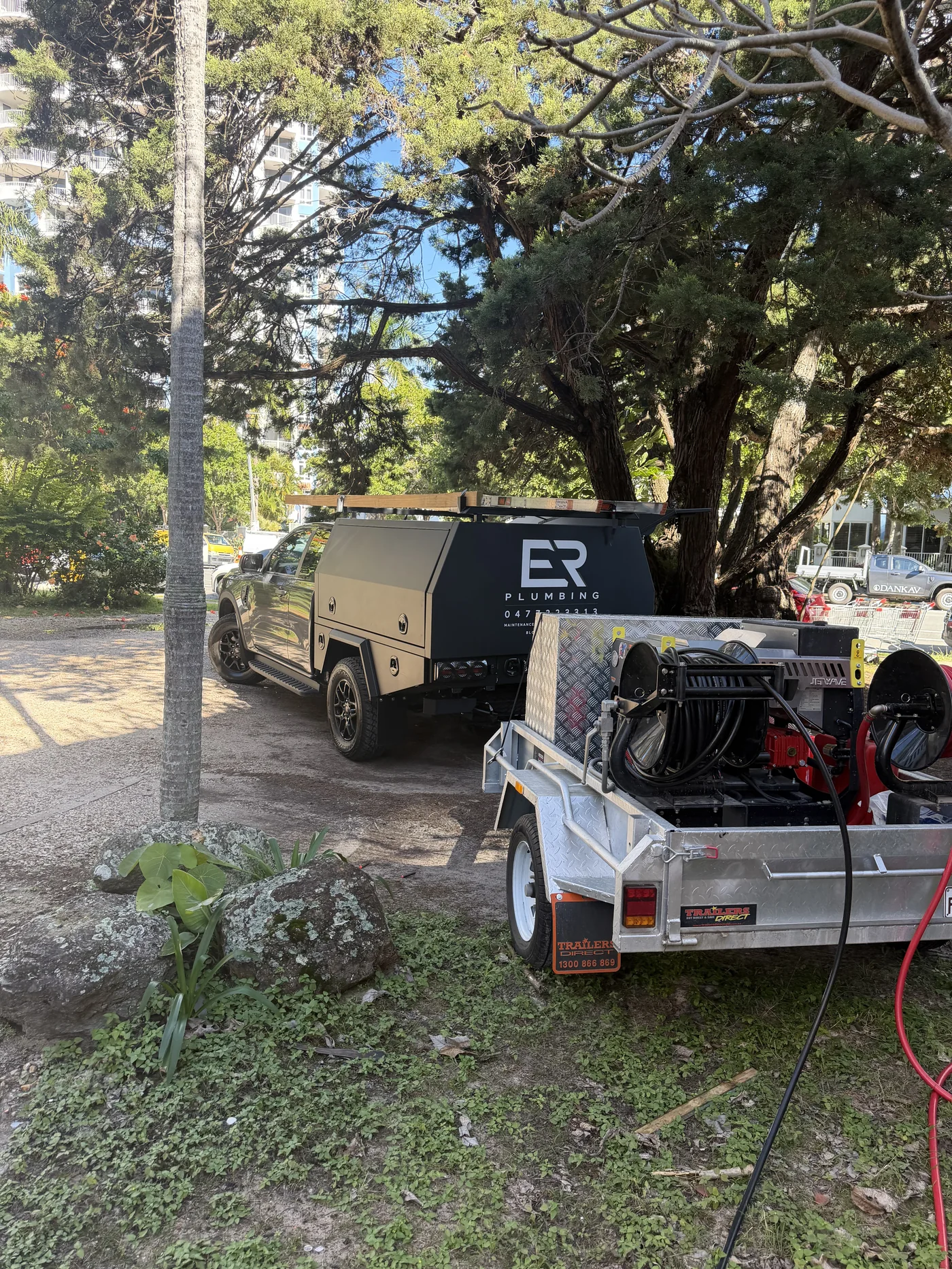 ER Plumbing ute with the jetting trailer hitched, parked under pine trees